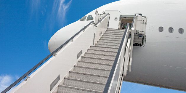 Looking up to the stairs reaching the business class of a commercial jet airplane used by boarding and disembarking passengers. White jetliner with blue sky.