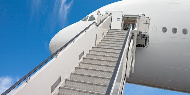 Looking up to the stairs reaching the business class of a commercial jet airplane used by boarding and disembarking passengers. White jetliner with blue sky.