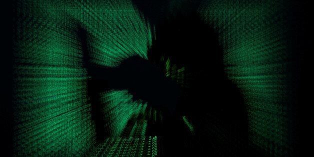 A hooded man holds laptop computer as cyber code is projected on him in this illustration picture taken on May 13, 2017. Capitalizing on spying tools believed to have been developed by the U.S. National Security Agency, hackers staged a cyber assault with a self-spreading malware that has infected tens of thousands of computers in nearly 100 countries. REUTERS/Kacper Pempel/Illustration