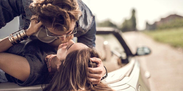 Young loving couple having a desire toward each other while lying on cabriolet.