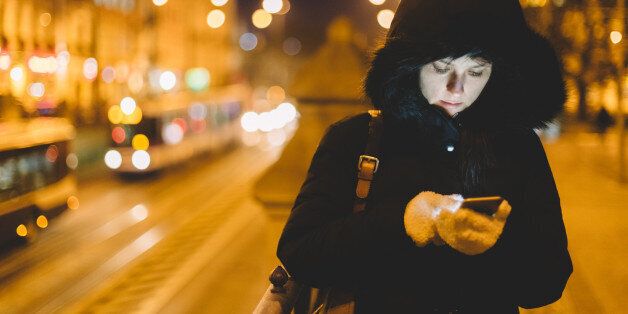 Woman in winter clothing texting in an urban scene.