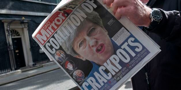 A television cameraman outside 10 Downing Street in London on June 10, 2017, reads a copy of The Daily Mirror newspaper with the headline 'Coalition of Crackpots' the day after the general election resulted in a hung parliament and British Prime Minister Theresa May forming a minority government. / AFP PHOTO / Justin TALLIS (Photo credit should read JUSTIN TALLIS/AFP/Getty Images)