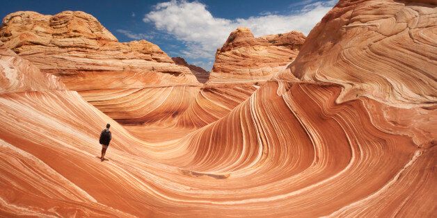 Adult male tourist hikes across the striated sandstone rock formations known as the Wave located within the Paria Canyon-Vermilion Cliffs Wilderness, Page, Arizona, US, North America