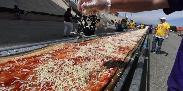Volunteers spread tomato sauce and cheese onto the pizza base as they successfully break the Guinness World Records title for Longest pizza with a length of 1.32 miles (2.13km) at the Auto Club Speedway track, in Fontana, California on June 10, 2017.A consortium of pizza oven makers and bakers joined forces to shatter the previous record from held by Napoli in Italy by 600 feet(182 metres). / AFP PHOTO / Mark RALSTON (Photo credit should read MARK RALSTON/AFP/Getty Images)