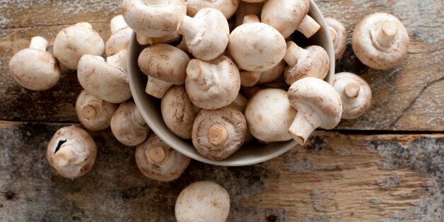 Fresh whole white button mushrooms, or agaricus, in a bowl on a rustic wooden counter ready to be cleaned and washed for dinner, overhead view