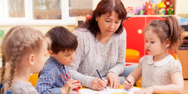 Kindergarten teacher, beautiful, mature caucasian woman, brown hair, teaches pupils drawing. Two little girls and a boy.