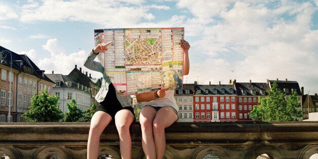 Two teenage girls sitting on bridge holding city map in front of them. Copenhagen city center.