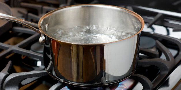 Water bubbles and boils on a gas stove or range in a home kitchen. Blue flame and stainless steel pot.
