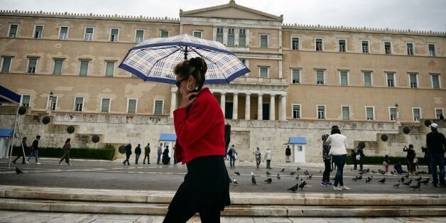 A woman walks past the Greek parliament as rain falls in Athens on October 27, 2016. Greece's top administrative court dealt a heavy blow to Prime Minister Alexis Tsipras by blocking his flagship reforms of the murky private television sector. Fourteen of the court's 25 judges said the controversial law passed in October 2015, limiting Greece to a maximum of four national private TV licences, was unconstitutional and should be overturned, a judicial source said. The government had auctioned off the licences for a total of 246 million euros ($268 million). But a majority of the judges ruled that it should have been up to Greece's independent broadcasting watchdog to carry out the reforms, not parliament. / AFP / LOUISA GOULIAMAKI (Photo credit should read LOUISA GOULIAMAKI/AFP/Getty Images)