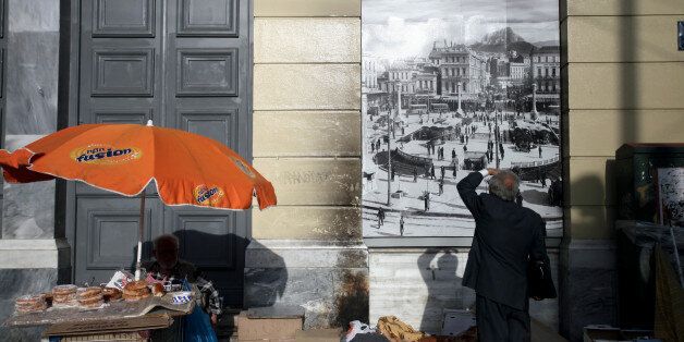 A man is looking an old image of Omonoia square next to a street vendor who sells bagels in Athens, Greece, May 11, 2017. (Photo by Giorgos Georgiou/NurPhoto via Getty Images)