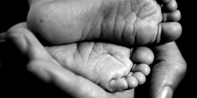 EDITORS PLEASE NOTE IMAGE CONVERTED TO BLACK AND WHITE A mother cradles the feet of her new born baby in her hand