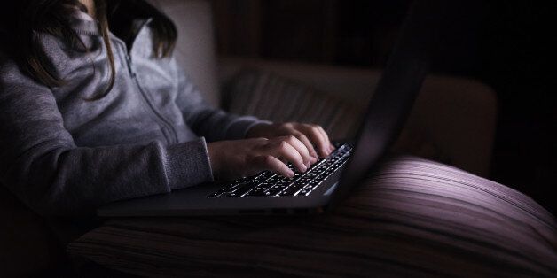 Unrecognizable girl, sitting in a dark, playing with laptop. Child at home, sitting on sofa.