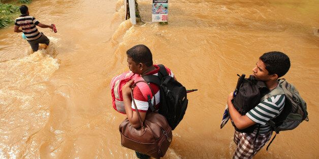 Two Sri Lankan men walk across a road inundated by floods with their belongings stored in backpacks following Flood warnings issued by government at Kaduwela, 20kms away from capital city Colombo, Sri Lanka. Friday 26th May 2017.More than 90 people were reported dead and hundreds were missing after heavy rains triggered floods and mudslides in Sri Lanka. (Photo by Tharaka Basnayaka/NurPhoto via Getty Images)