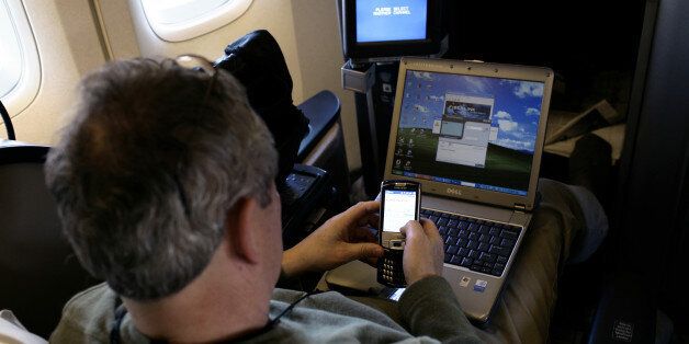 A passenger uses a laptop computer and mobile phone inside of a commercial passenger 747-400 airplane. (Photo by Brooks Kraft LLC/Corbis via Getty Images)