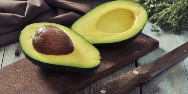 Fresh avocado on cutting board over wooden background