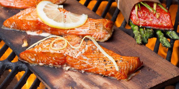 Three wild-caught salmon filets on a cedar plank in a backyard grill. Fist is bright reddish orange and is topped with lemon, dill and cracked pepper file_thumbview_approve.php?size=1&id=19631280