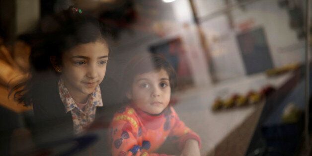 Syrian refugee children from the Abdulwahed family look out to the curling rink as it is reflected in the glass at the Royal Canadian Curling Club, during an event where refugees were introduced to the sport of curling put on by the