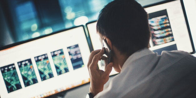 Rear view of partially unrecognizable male software developer creating different interfaces for certain application. He's on the phone line with the client at the same time.