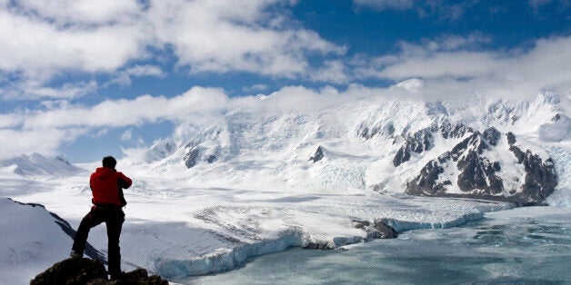 Mountaineer standing on a rock in front of a picturesque mountain range on Livingston Island, Antarctica. The range rises about 1800 meters above the sea level. The highest peak is known as Friesland.