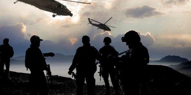 Silhouette of soldiers and helicopters during a military mission at dusk.