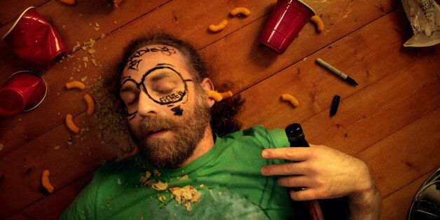 Man passed out at party laying on floor clutching bottle with stuff drawn on his face.