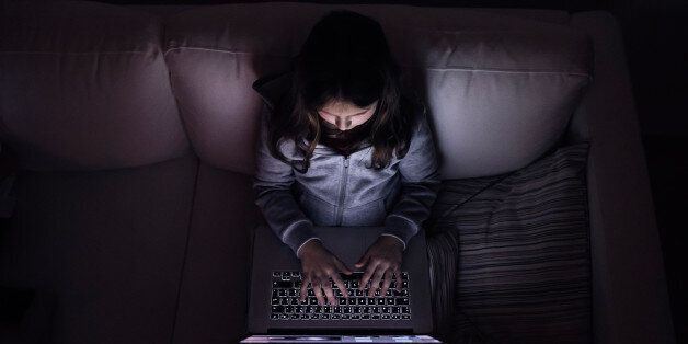 Little girl, sitting in a dark, playing with laptop. Child at home, sitting on sofa.