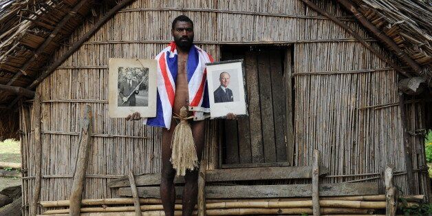 TO GO WITH AFP STORY 'Vanuatu-Britain-religion-royals,FEATURE' by Madeleine Coorey Sikor Natuan, the son of the local chief, holds two official portraits (one holding a pig-killing club, L) of Britain's Prince Philip in front of the chief's hut in the remote village of Yaohnanen on Tanna in Vanuatu on August 6, 2010. In his remote village in Vanuatu, tribesman Sikor Natuan cradles a faded portrait of Britain's Prince Philip against his naked and tattooed chest. Natuan, who just weeks before danced and feasted to mark the royal's 89th birthday, is already preparing for next year's celebrations -- and he is expecting the guest of honour to attend, despite his advanced age. For in the South Pacific village of Yaohnanen on Vanuatu's Tanna island, where men wear nothing but grass penis sheaths, and marijuana and tobacco grow wild, Prince Philip is worshipped as a god. AFP PHOTO / Torsten BLACKWOOD (Photo credit should read TORSTEN BLACKWOOD/AFP/Getty Images)