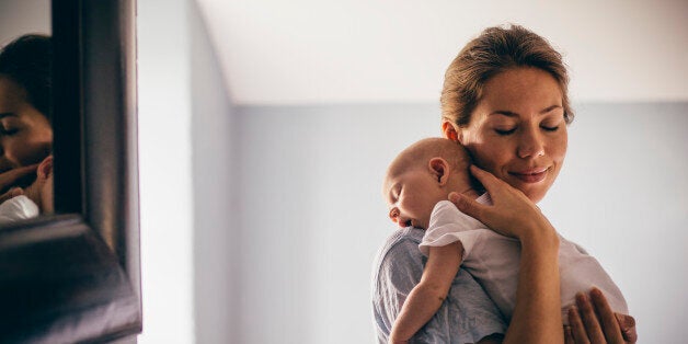 A happy new mother smiles as she craddles her sleeping baby in her arms. She has her eyes closed as she holds her close.