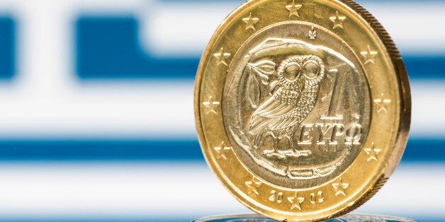 Close-up of a Greek flag and a Greek euro coin. Focus is on the Greek euro.