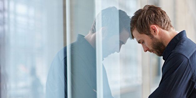 Young businessman looking depressed leaning his head against a window