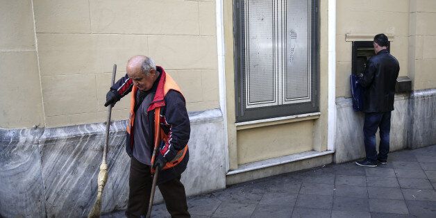 A municipal worker sweeps the sidewalk as a customer uses an automated teller machine (ATM) outside an Alpha Bank SA bank branch in Athens, Greece, on Tuesday, Feb. 28, 2017. Greeces auditors are pulling together a list of policies the country needs to implement to unlock additional bailout funds as talks with Athens resumed on Tuesday, two people familiar with the matter said. Photographer: Yorgos Karahalis/Bloomberg via Getty Images