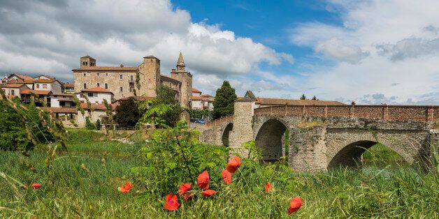Roman Bridge, people, river, houses and Church of Monastero Bormida in Piedmont, Italy.