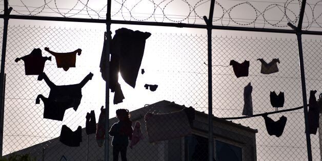 Children dry their laundry behind a fence at the VIAL detention center on the island of Chios where migrants and refugees arrived after the March 20 EU-Turkey deal are kept, on April 4, 2016. Greece sent a first wave of migrants back to Turkey on April 4 under an EU deal that has faced heavy criticism from human rights defenders. Under the agreement, designed to halt the main influx which comes from Turkey, all 'irregular migrants' arriving since March 20 face being sent back, although the deal calls for each case to be examined individually. For every Syrian refugee returned, another Syrian refugee will be resettled from Turkey to the EU, with numbers capped at 72,000. / AFP / LOUISA GOULIAMAKI (Photo credit should read LOUISA GOULIAMAKI/AFP/Getty Images)