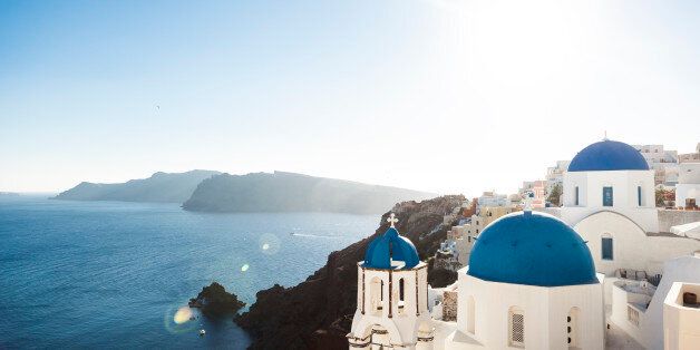 The church domes of Santorini in the village of Oia. The first one is 'Agios Spyridonas', St. Spyridonas church. The name of the second blue dome in the background is 'Anastaseos' that means resurrection of Christ. Caldera with volcanic islands in the background. Backlit with sunflare.