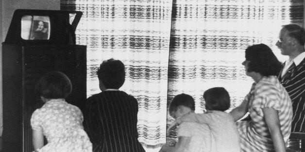 UNITED KINGDOM - FEBRUARY 23: A family watching a television broadcast, c 1930s. Photograph showing a family watching a television programme on a mirror lid television. When switched on, the image on the horizontal 12 inch screen was reflected onto, and viewed via, the mirror on the lid of the case. This early television set used magnetic deflection and electrostatic focusing. (Photo by Daily Herald Archive/SSPL/Getty Images)