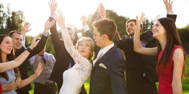 Full length portrait of newlywed couple dancing and having fun with bridesmaids and groomsmen in green sunny park