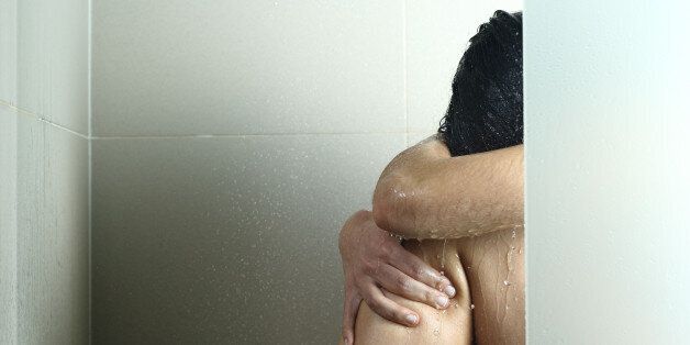 Sad woman after abuse crying under the water in the shower