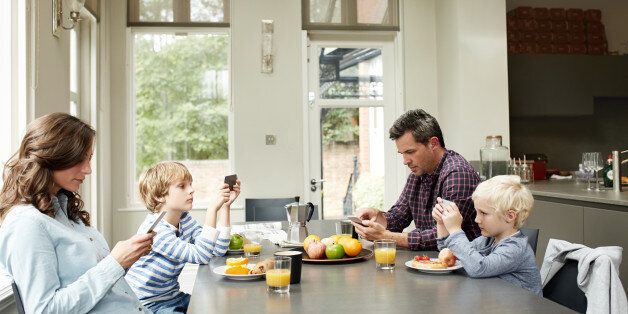 Shot of a family of four distracted by their cellphones while eating breakfast together