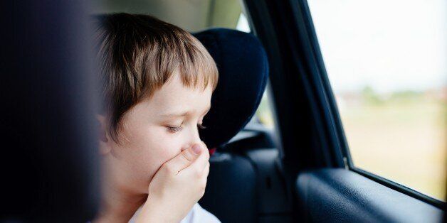 Seven years old small child in the backseat of a car sitting in children safety car seat covers his mouth with his hand - suffers from motion sickness