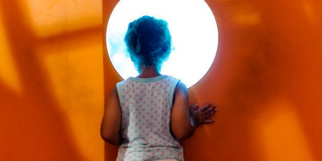 Cstock photo of little girl who is looking through a hole in a wall. She is looking into an aquarium. This file has a signed model release.