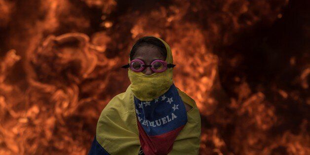 CARACAS, VENEZUELA - APRIL 24: Venezuelan opposition activist cover his face in front of burning barricades as the protesters block a main highway during a march against the government of President NIcolas Maduro, in Caracas, on April 24, 2017. Venezuela is grappling with a new wave of political protest since April 4 that has led to the deaths of 21 people. (Photo by Carlos Becerra/Anadolu Agency/Getty Images)