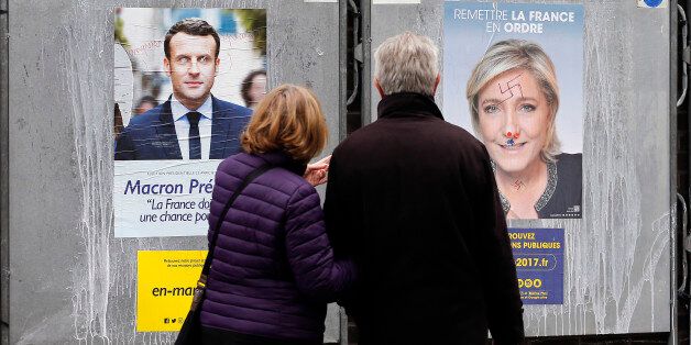 PARIS, FRANCE - APRIL 18: A couple look at graffitied official campaign posters of Marine Le Pen, French National Front (FN) and political party leader and Emmanuel Macron, head of the political movement En Marche! (On move !), two of the eleven candidates who runs in the 2017 French presidential election on April 18, 2017 in Paris, France. French 2017 presidential election which will take place on April 23 and May 07, 2017. (Photo by Chesnot/Getty Images)
