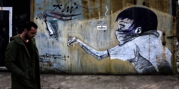 TOPSHOT - A man walks past a graffiti depicting a man throwing a petrol bomb on March 17, 2017 in the Greek capital, Athens.Greek authorities on March 17, 2017 were trying to determine how a near-defunct militant group was able to sneak at least two parcel bombs through airport security, one of which exploded at the IMF offices in Paris. The investigation so far suggests that the booby-trapped mail sent to the IMF and the German finance ministry -- presumably by a far-left group called the Conspiracy of Fire Nuclei -- failed to raise an alarm because it contained only a small amount of gunpowder. / AFP PHOTO / Angelos Tzortzinis (Photo credit should read ANGELOS TZORTZINIS/AFP/Getty Images)