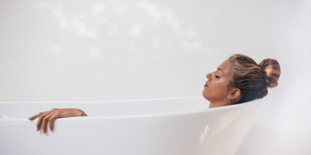 Side view shot of young woman lying in bathtub with her eyes closed. Female relaxing in bathtub.