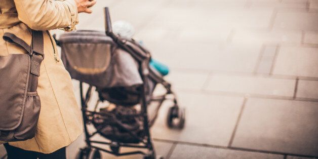 Photo of modern mom pushing a buggy on the street and holding cup of coffee