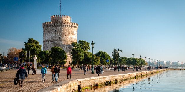 Thessaloniki, Greece - December 24, 2015: People walking on the coast in Thessaloniki next to the white tower which once guarded the eastern end of the city's sea walls
