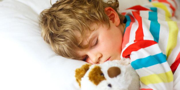 Adorable little blond kid boy in colorful nightwear clothes sleeping and dreaming in his white bed with toy. healthy child with soft toy, peaceful sleep at home.