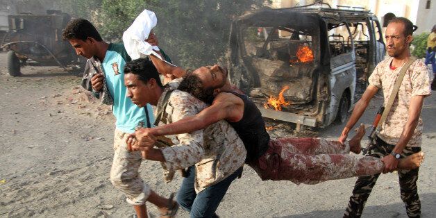 TOPSHOT - EDITORS NOTE: Graphic content / Yemenis carry a wounded man past a burning vehicle following a reported suicide car bombing in Huta, the capital of the southern province of Lahj, a bastion of Al-Qaeda jihadists, on March 27, 2017.Ten jihadists, including a suicide bomber, perished when they attacked a government building in southern Yemen, killing six soldiers and four civilians, officials said. / AFP PHOTO / SALEH AL-OBEIDI (Photo credit should read SALEH AL-OBEIDI/AFP/Getty Images)