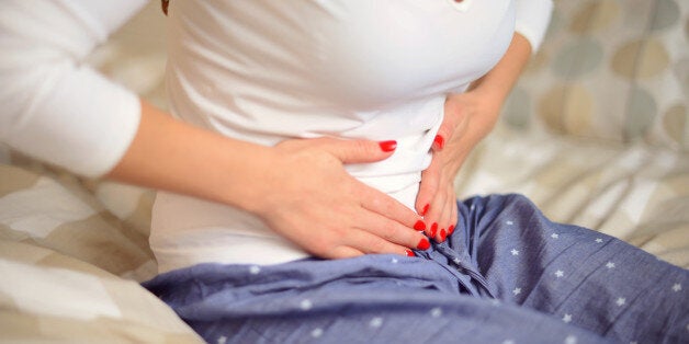 young woman sitting in the bedroom on a bed and holding her stomach,abdominal pain