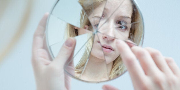 Insecure pretty young woman holding broken mirror